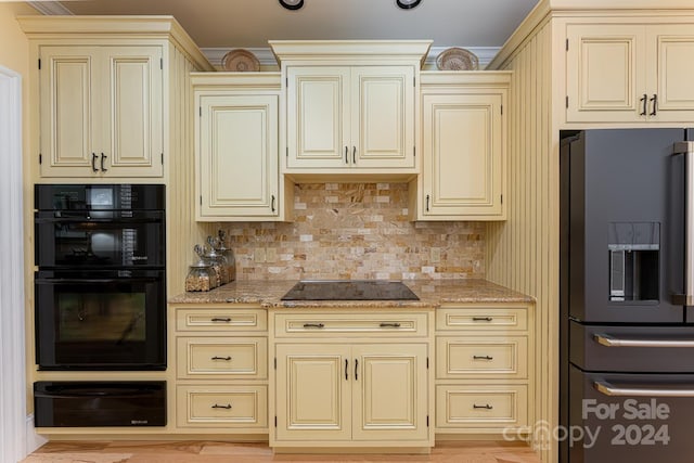 kitchen featuring cream cabinetry, light stone countertops, and black appliances