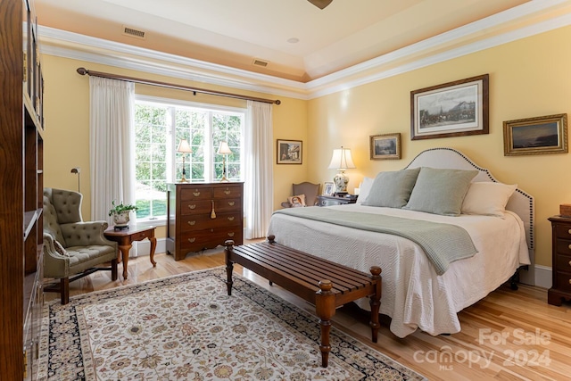 bedroom with wood-type flooring, a raised ceiling, and ornamental molding