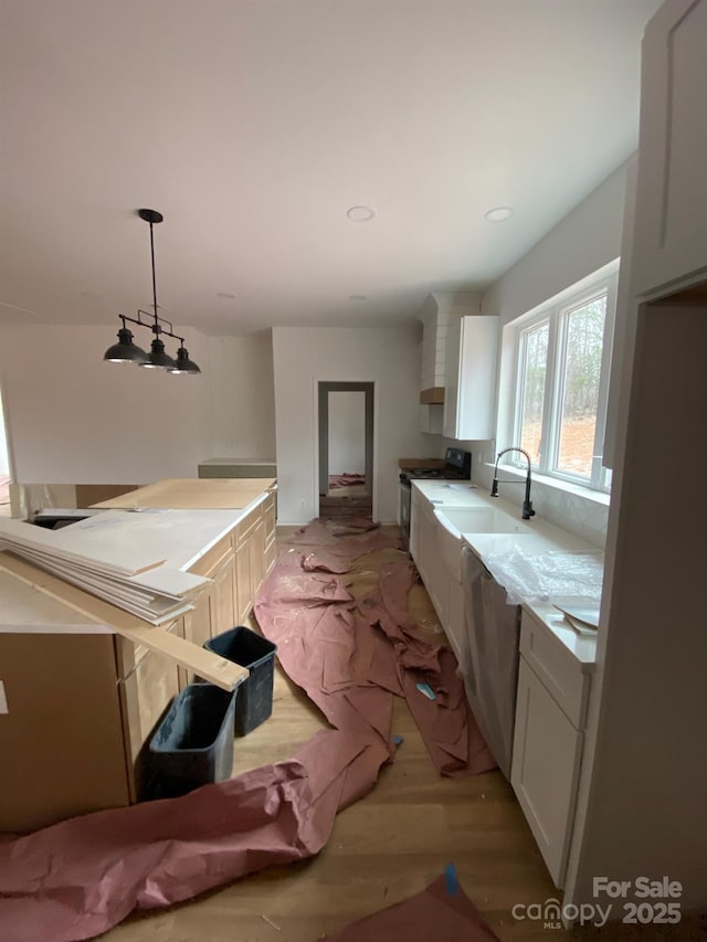 kitchen with stainless steel range oven, sink, white cabinetry, decorative light fixtures, and light hardwood / wood-style floors