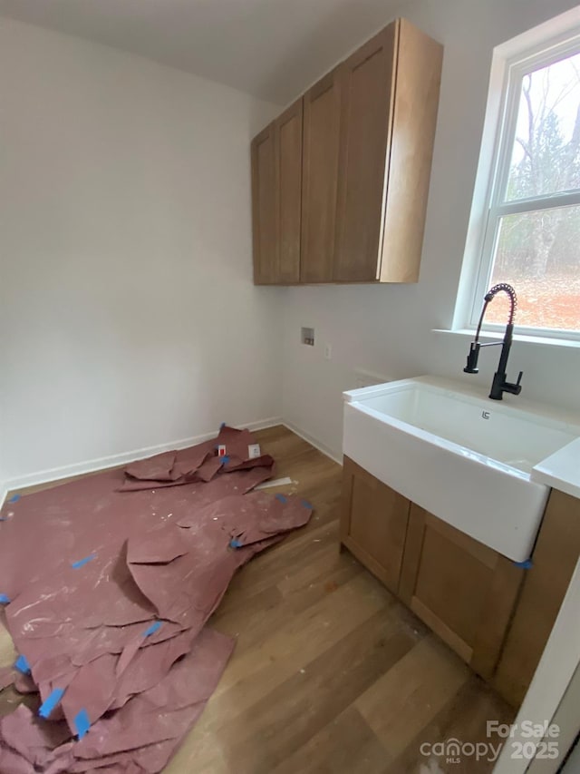 clothes washing area with washer hookup, sink, light hardwood / wood-style floors, and cabinets