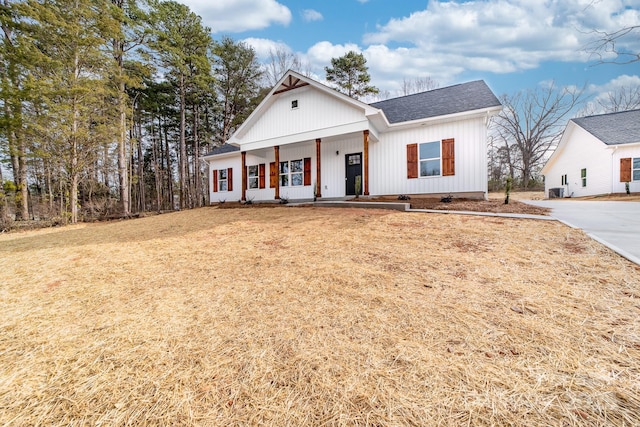 modern farmhouse style home with a porch, a front lawn, and roof with shingles