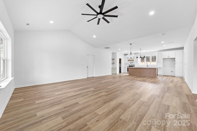 unfurnished living room with vaulted ceiling, recessed lighting, ceiling fan with notable chandelier, and light wood-style floors
