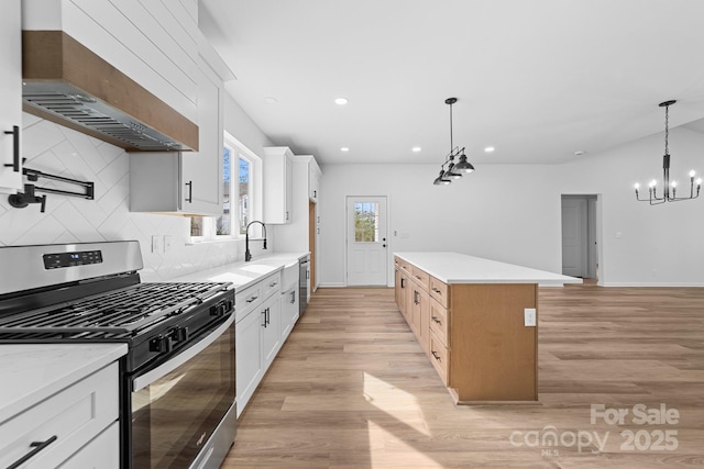 kitchen with stainless steel range with gas cooktop, light wood-type flooring, decorative backsplash, a notable chandelier, and wall chimney exhaust hood