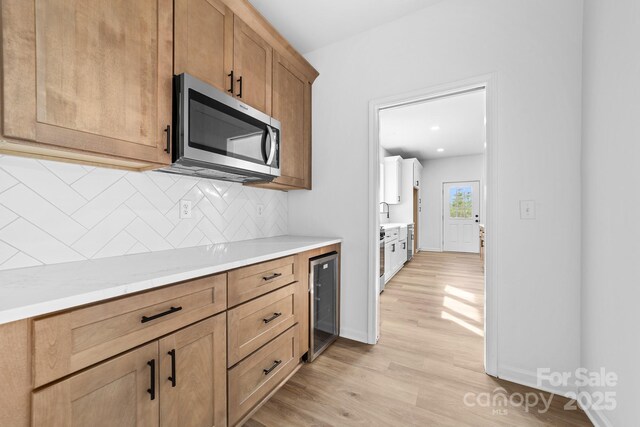 kitchen featuring light countertops, wine cooler, stainless steel microwave, light wood-type flooring, and backsplash