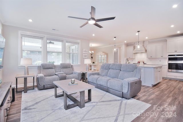 living room featuring ceiling fan with notable chandelier, light hardwood / wood-style floors, ornamental molding, and sink