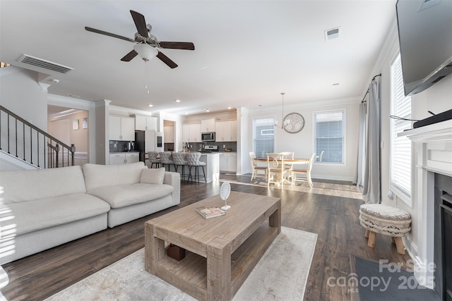 living room featuring ceiling fan with notable chandelier, dark hardwood / wood-style floors, and crown molding