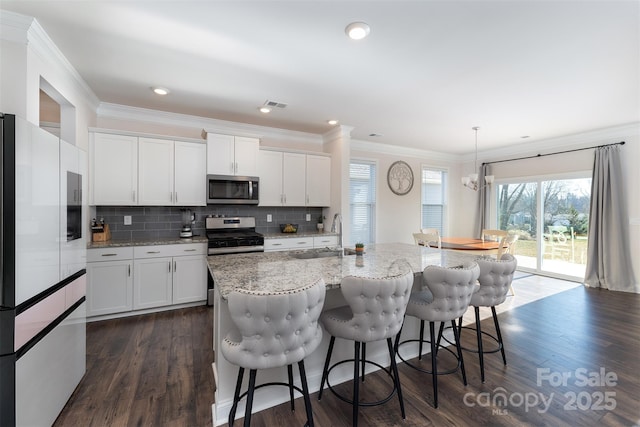 kitchen with white cabinets, decorative light fixtures, stainless steel appliances, and an island with sink