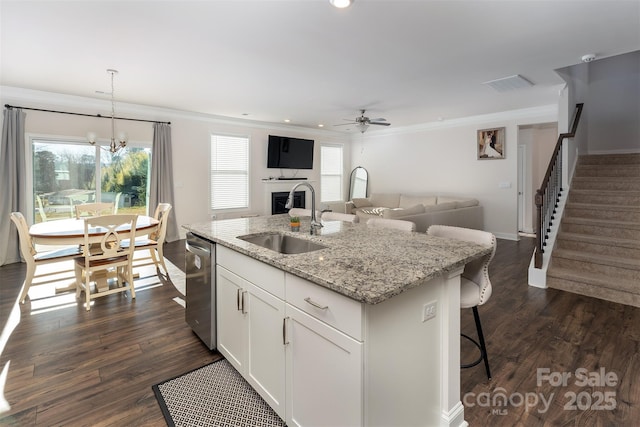 kitchen with light stone countertops, ceiling fan with notable chandelier, sink, a center island with sink, and white cabinetry