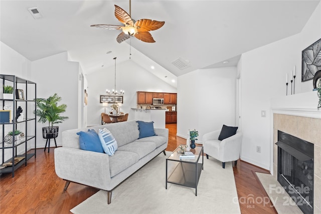 living room with a tiled fireplace, high vaulted ceiling, ceiling fan with notable chandelier, and hardwood / wood-style flooring