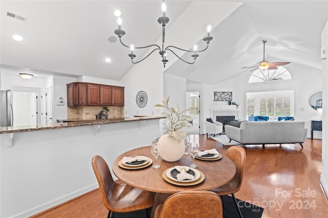 dining space with ceiling fan with notable chandelier, light wood-type flooring, lofted ceiling, and a tiled fireplace