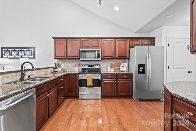 kitchen with dark stone counters, sink, decorative backsplash, light wood-type flooring, and stainless steel appliances