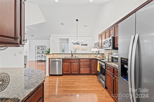 kitchen with lofted ceiling, dark stone counters, sink, decorative light fixtures, and stainless steel appliances