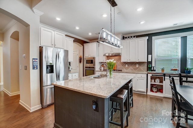 kitchen featuring arched walkways, white cabinets, an island with sink, appliances with stainless steel finishes, and a sink