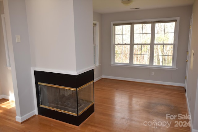 unfurnished living room with a multi sided fireplace, wood-type flooring, and a wealth of natural light