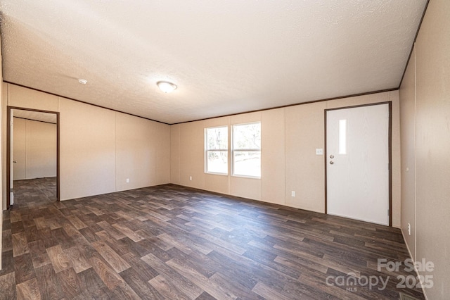 spare room featuring crown molding, dark wood-type flooring, and a textured ceiling