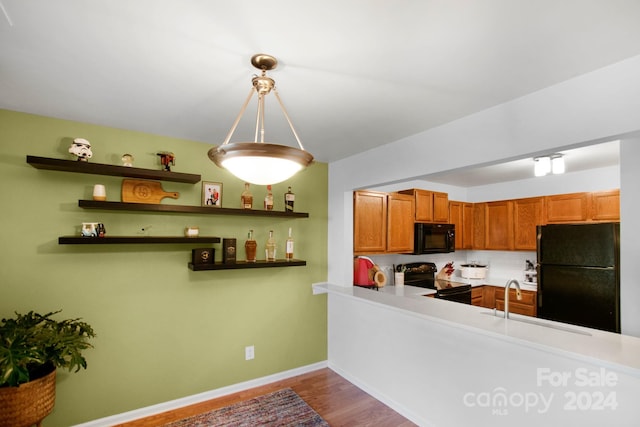 kitchen with pendant lighting, black appliances, wood-type flooring, sink, and kitchen peninsula