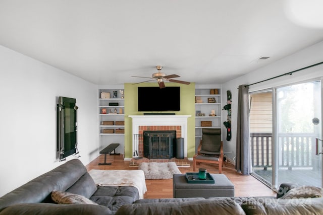 living room featuring built in shelves, light hardwood / wood-style flooring, and ceiling fan