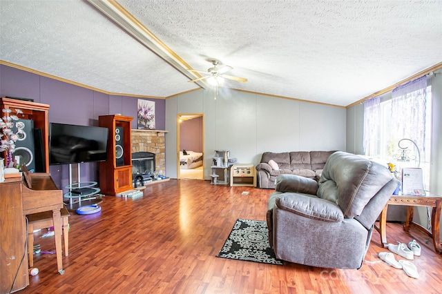 living room featuring vaulted ceiling, hardwood / wood-style flooring, ornamental molding, a fireplace, and a textured ceiling