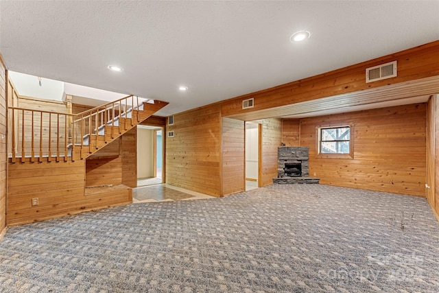 unfurnished living room featuring a stone fireplace, wooden walls, carpet, and a textured ceiling