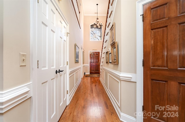 hallway with light wood-type flooring, crown molding, and an inviting chandelier