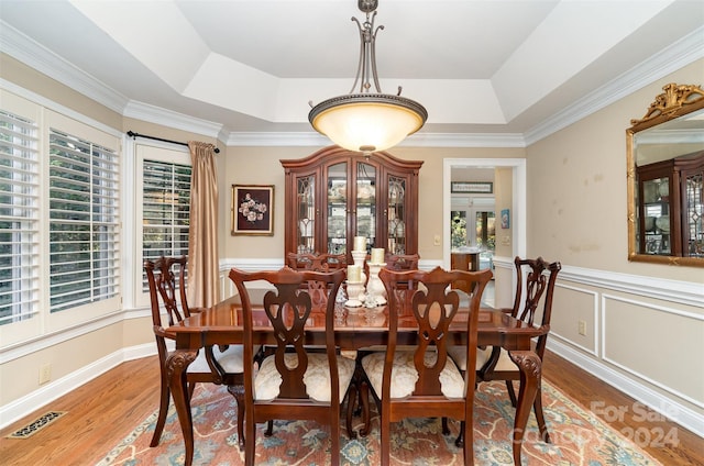 dining area with hardwood / wood-style floors, a raised ceiling, and ornamental molding