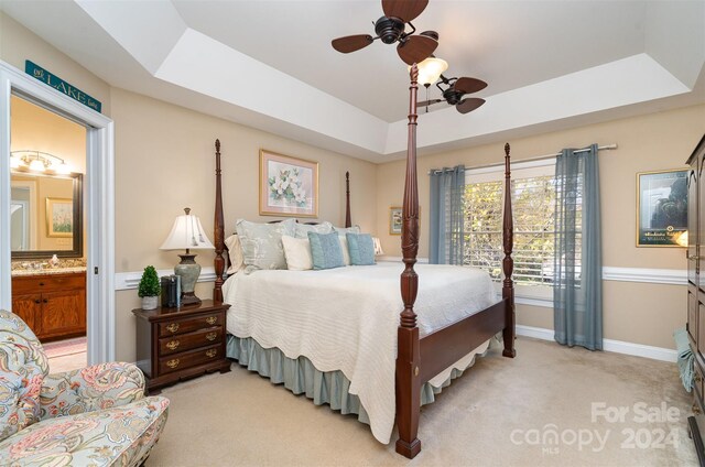 carpeted bedroom featuring connected bathroom, a raised ceiling, and ceiling fan