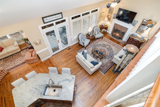 living area featuring french doors, wood finished floors, a brick fireplace, baseboards, and visible vents