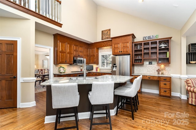 kitchen with stainless steel appliances, brown cabinetry, light wood-type flooring, and open shelves