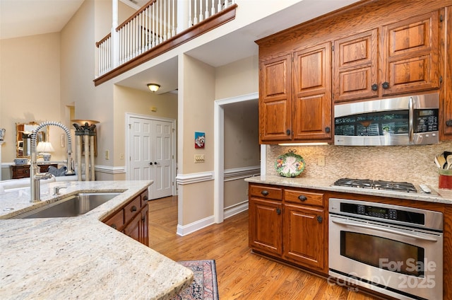 kitchen featuring stainless steel appliances, a sink, light wood-style floors, light stone counters, and brown cabinetry