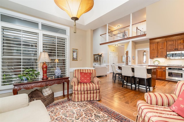 living area with baseboards, light wood-style floors, and a towering ceiling