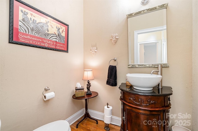 half bath featuring baseboards, toilet, wood finished floors, and vanity