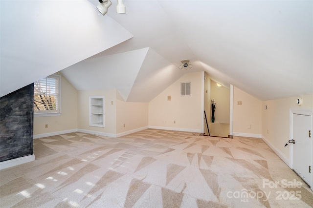 additional living space with baseboards, visible vents, built in shelves, and light colored carpet