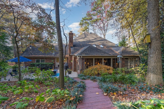back of property with a wooden deck, brick siding, and a chimney