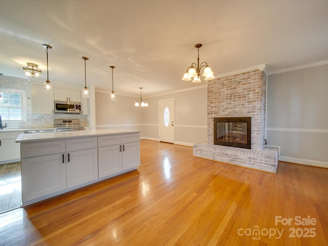 kitchen with white cabinetry, stainless steel appliances, a brick fireplace, backsplash, and pendant lighting