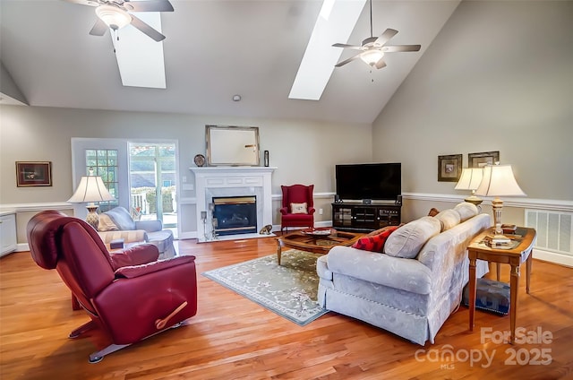 living room with ceiling fan, a skylight, and light hardwood / wood-style flooring