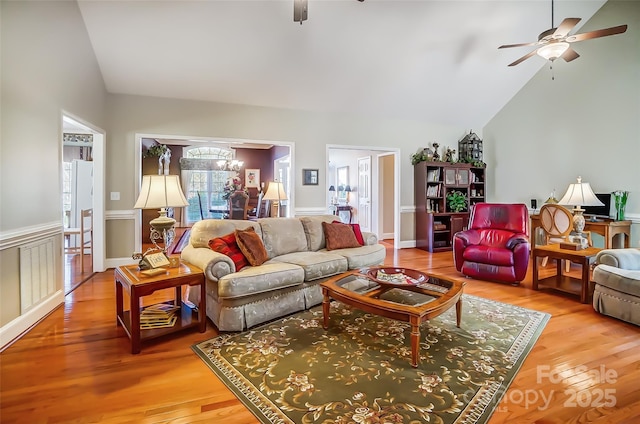 living room with high vaulted ceiling, ceiling fan with notable chandelier, and hardwood / wood-style flooring