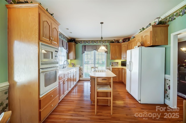 kitchen with white appliances, hanging light fixtures, a center island, and light hardwood / wood-style flooring