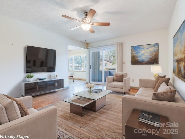 living room featuring ceiling fan, light hardwood / wood-style floors, and a textured ceiling