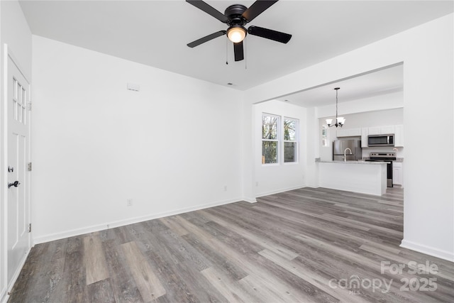 unfurnished living room featuring ceiling fan with notable chandelier and light hardwood / wood-style floors