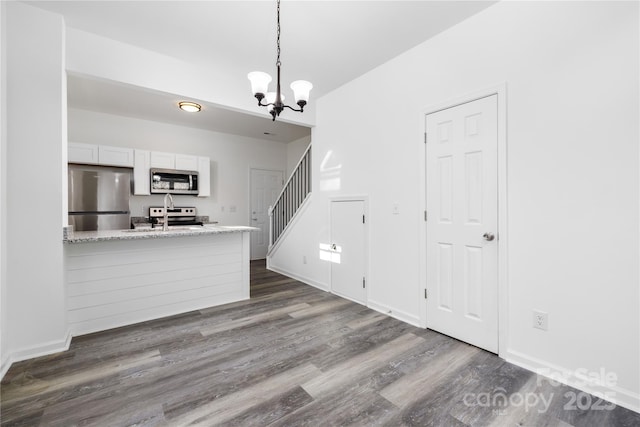 kitchen featuring white cabinetry, light stone counters, an inviting chandelier, hanging light fixtures, and stainless steel appliances