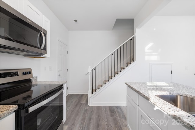 kitchen featuring light stone counters, appliances with stainless steel finishes, light wood-type flooring, and white cabinets