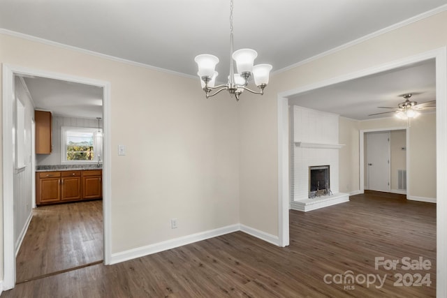 unfurnished living room with crown molding, dark hardwood / wood-style flooring, ceiling fan with notable chandelier, and a brick fireplace