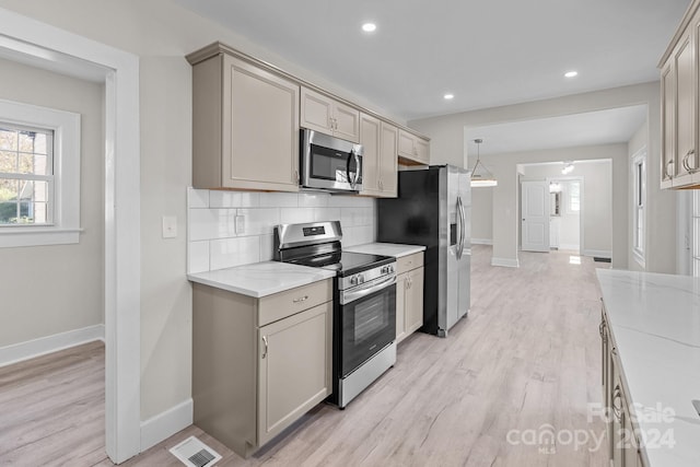 kitchen with backsplash, light stone counters, light wood-type flooring, and stainless steel appliances