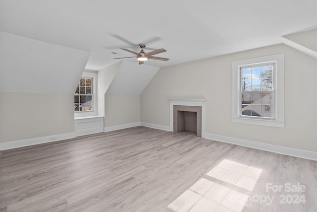 additional living space with a brick fireplace, light wood-type flooring, vaulted ceiling, and ceiling fan