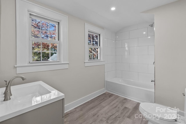 full bathroom with vanity, vaulted ceiling, hardwood / wood-style flooring, tiled shower / bath combo, and toilet