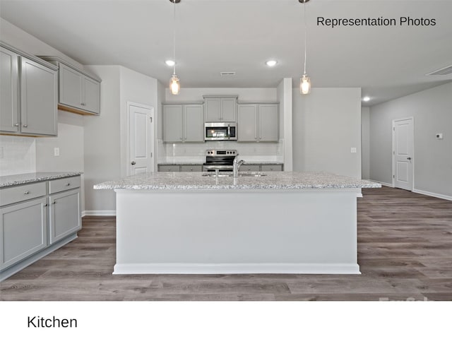 kitchen featuring pendant lighting, hardwood / wood-style flooring, stainless steel appliances, and a kitchen island with sink