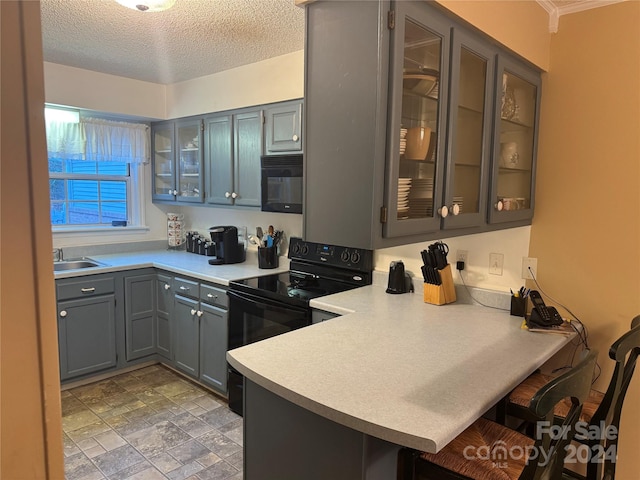 kitchen with a breakfast bar, black appliances, sink, a textured ceiling, and kitchen peninsula