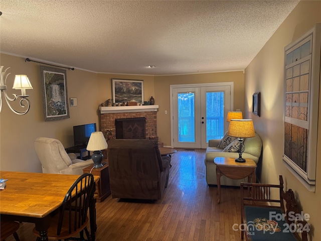 living room featuring dark wood-type flooring, french doors, crown molding, a brick fireplace, and a textured ceiling