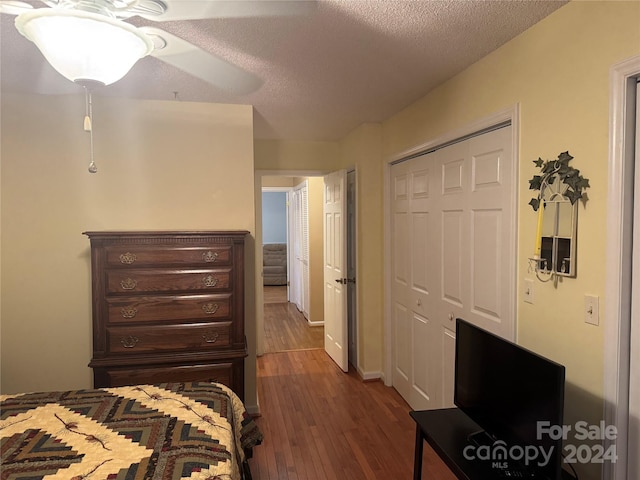 bedroom featuring a textured ceiling, dark hardwood / wood-style flooring, a closet, and ceiling fan