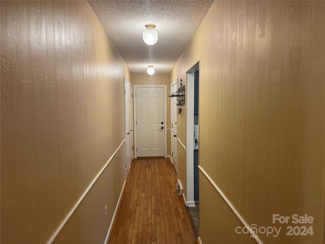 corridor with wood-type flooring, a textured ceiling, and wooden walls